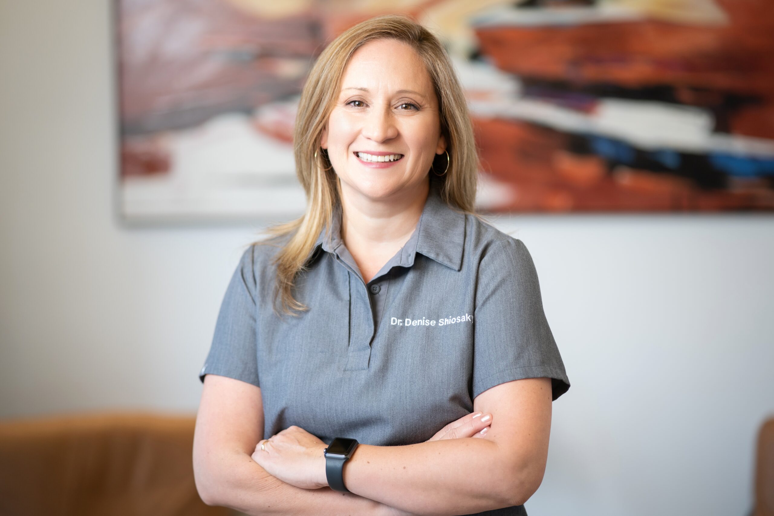 Dr. Shiosaky, a smiling female dentist sign while standing in front of colorful abstract artwork at Mission Dental Studio